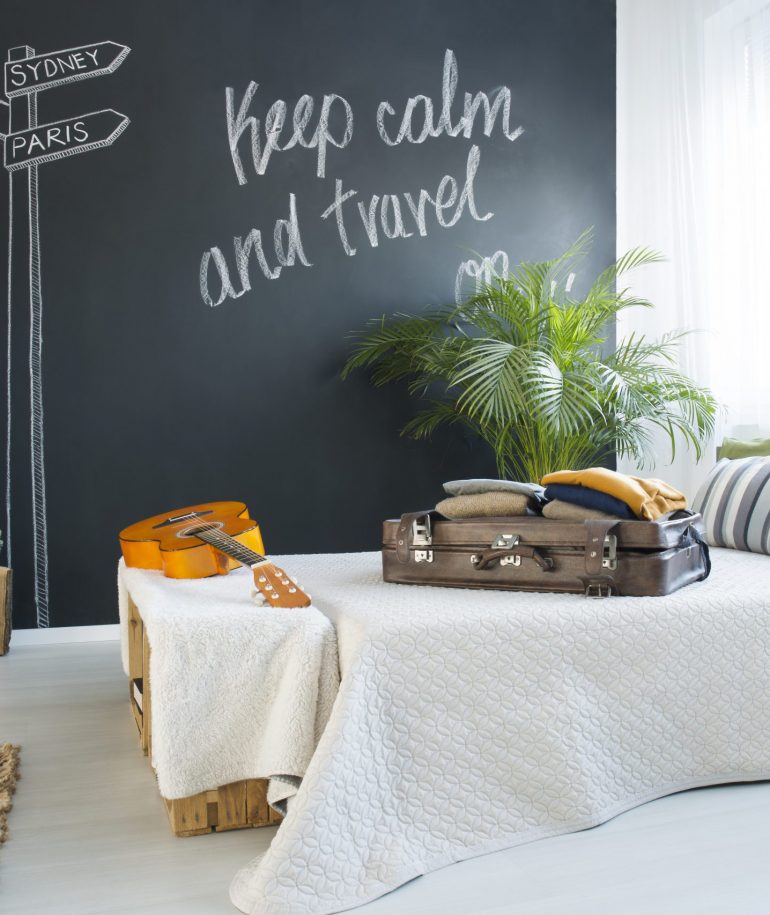 Bed in modern travel-themed bedroom with blackboard wall