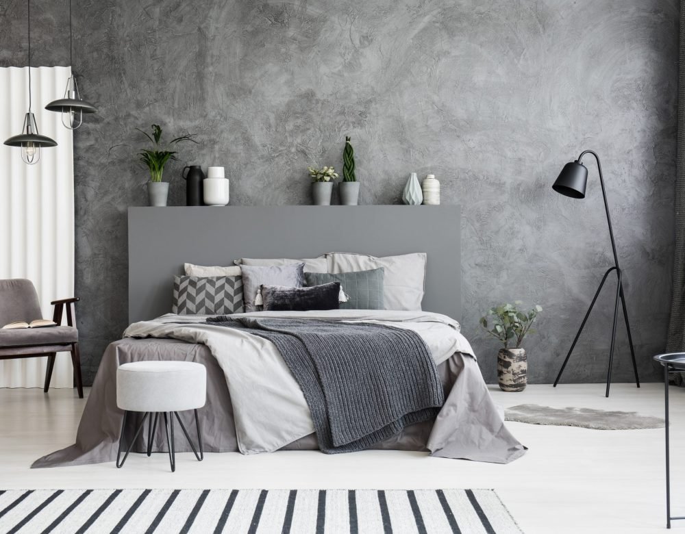 Grey armchair and stool near bed with headboard in bedroom inter Grey armchair and stool near bed with headboard in bedroom interior with black lamp. Real photo