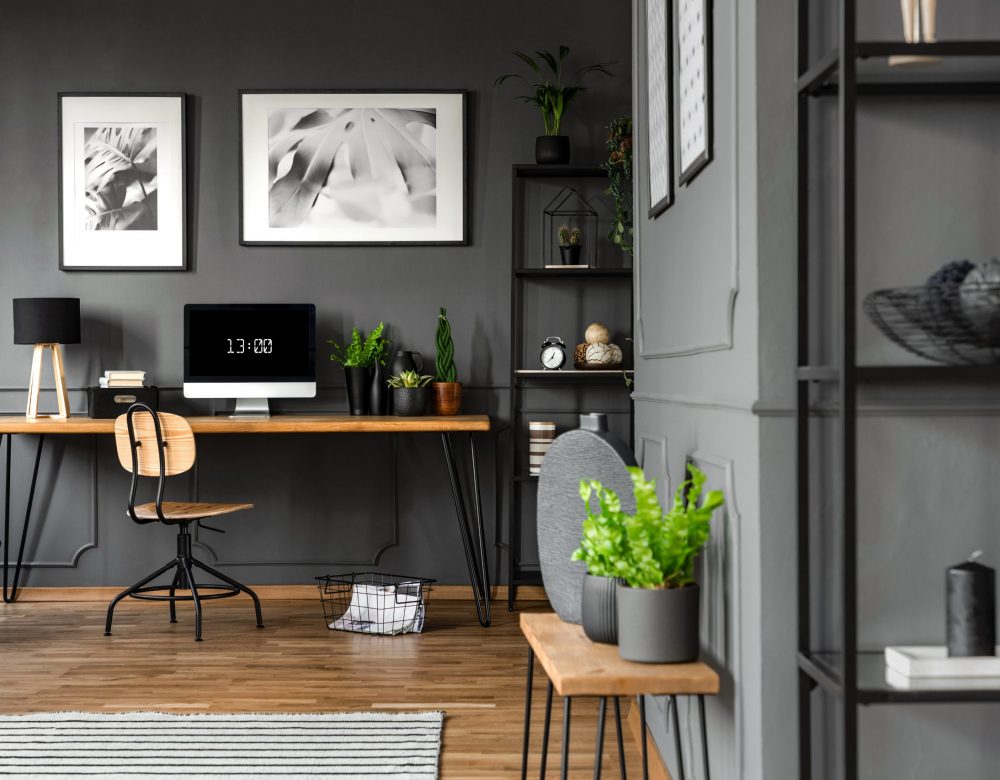 Plants on wooden table in grey home office interior with posters above desk with computer monitor